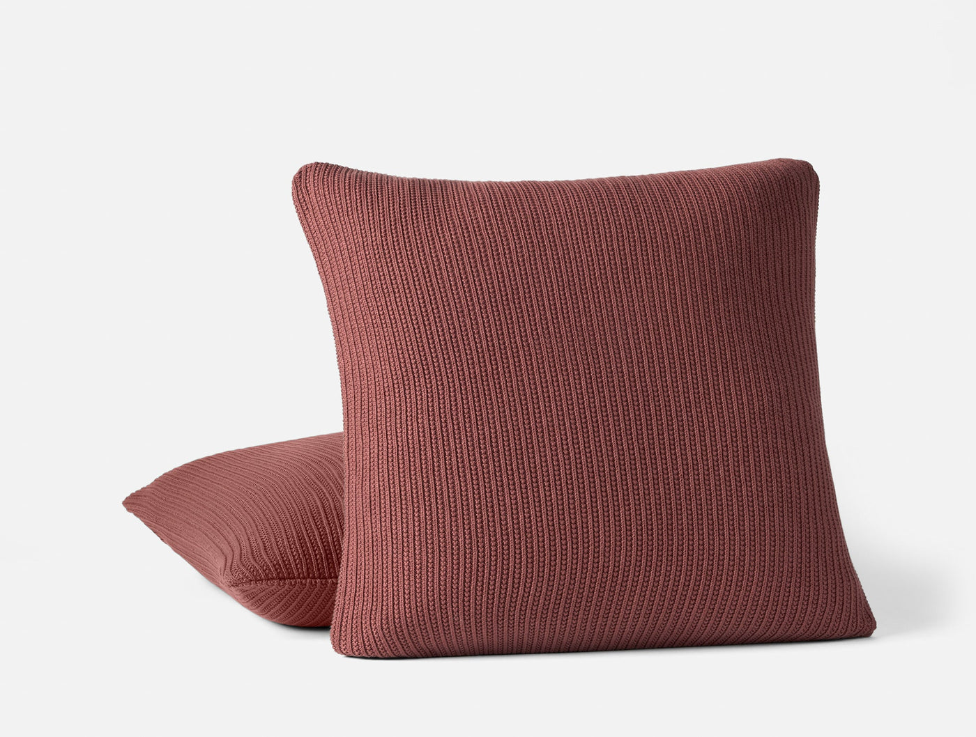 Two Coyuchi Linea Knit pillows in terracotta, ribbed texture, stacked on white background.