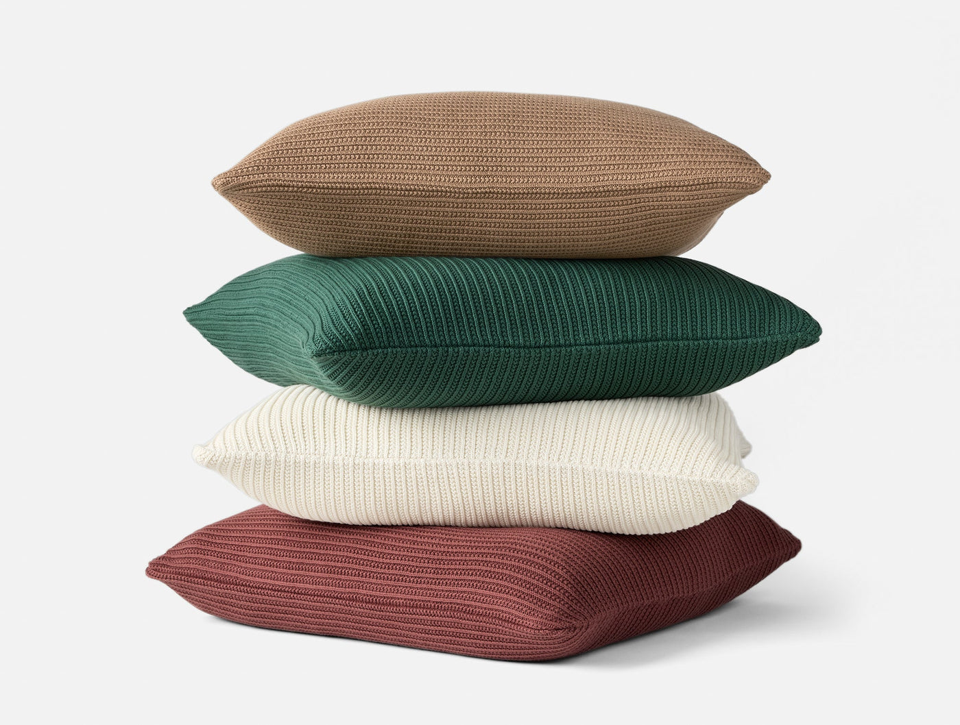 Four stacked Coyuchi Linea Knit pillows in tan, green, ivory, and burgundy ribbed knit.