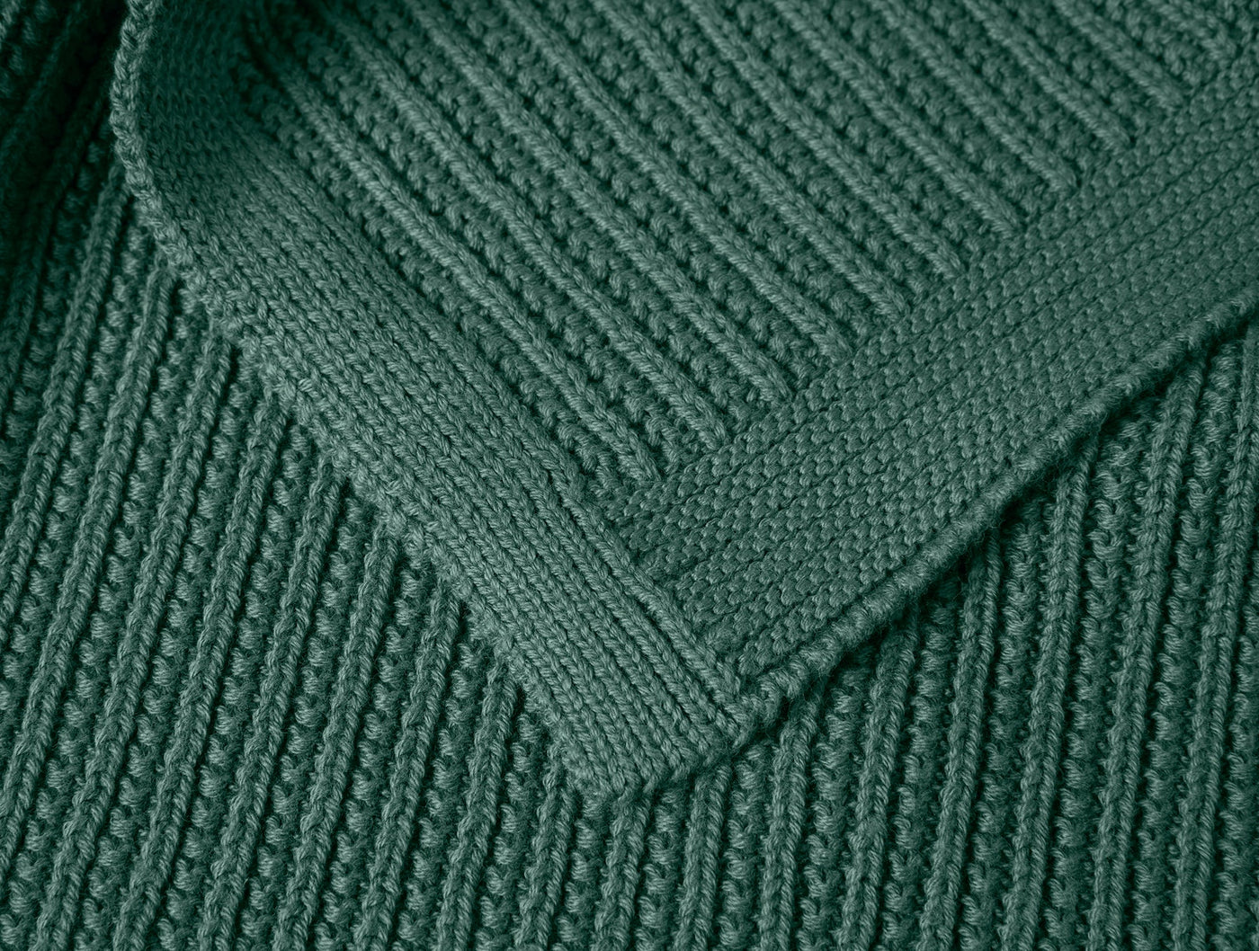 Close-up of folded corner showing forest green ribbed knit texture and finished edge.