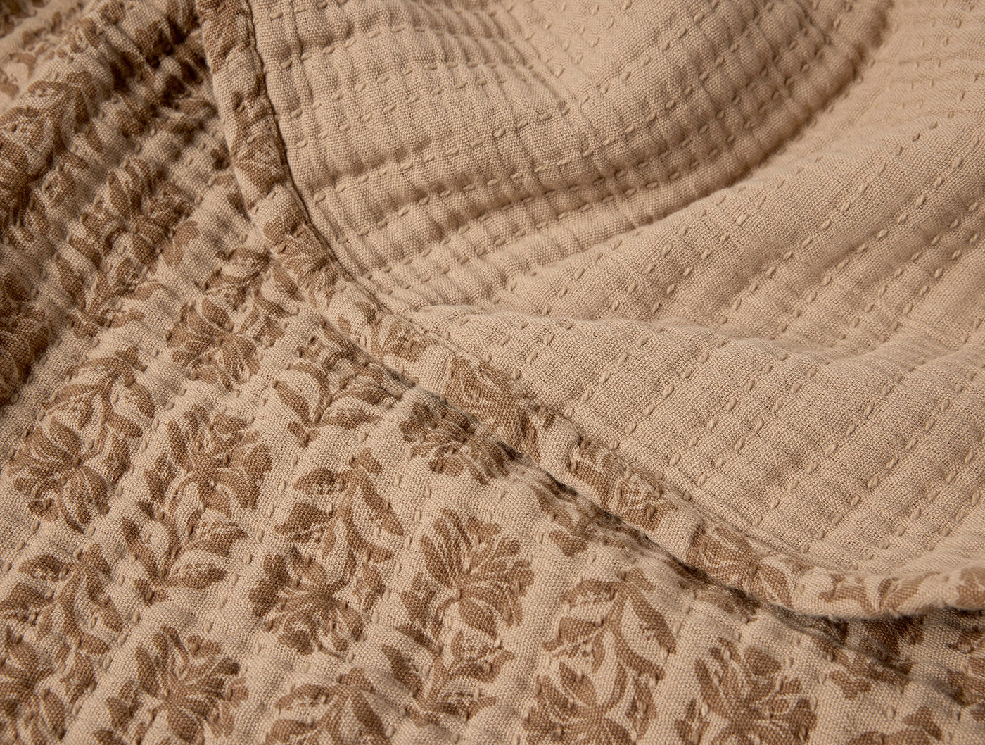 Close-up of Coyuchi Mirada Matelassé blanket in taupe, showing floral jacquard and quilted textures.