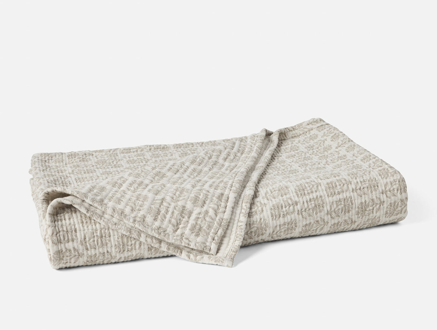 Close-up of folded Coyuchi Mirada Matelasse blanket in natural grey textured weave.