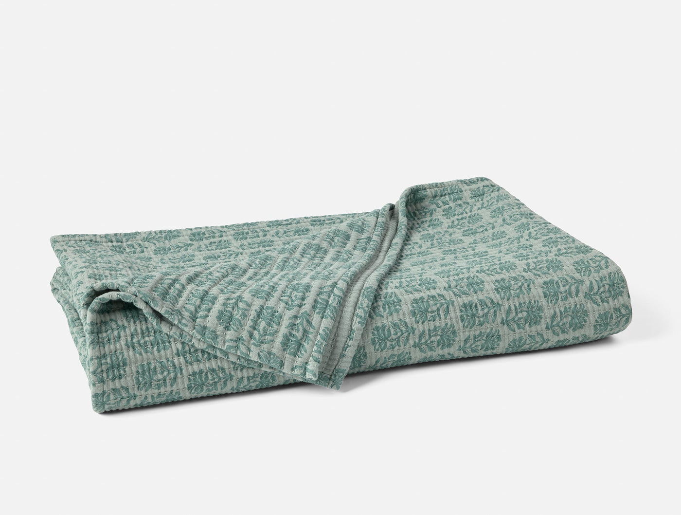 Folded sage green matelassé blanket showing botanical jacquard pattern and texture.