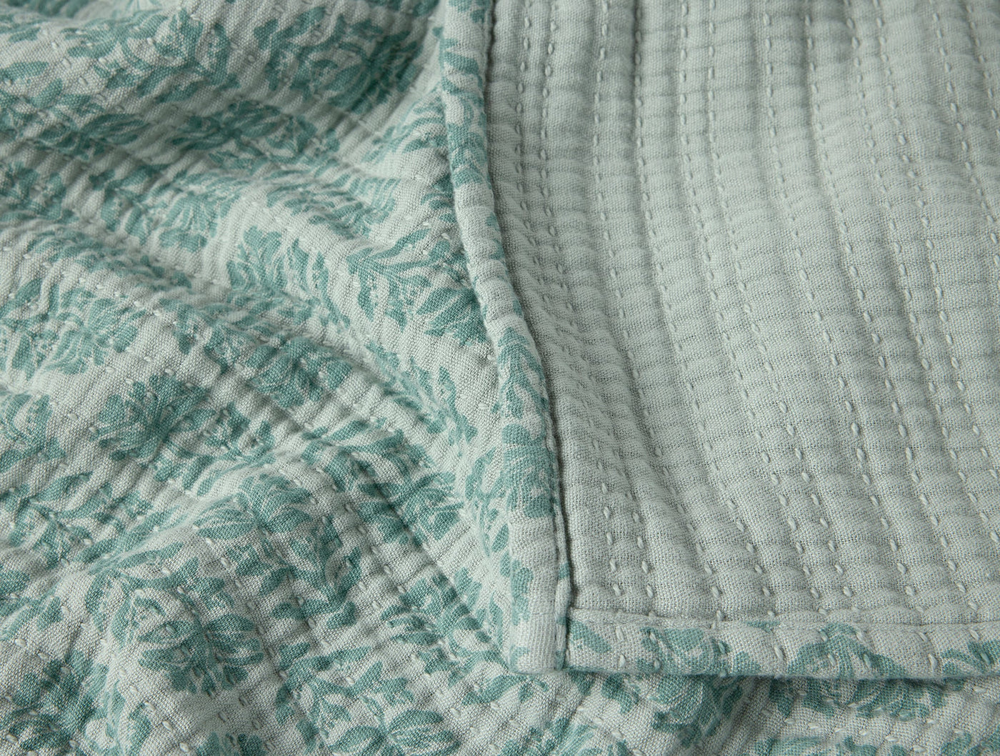 Close-up of Coyuchi Mirada Matelassé throw in seafoam, showing block-print floral and quilted reverse.