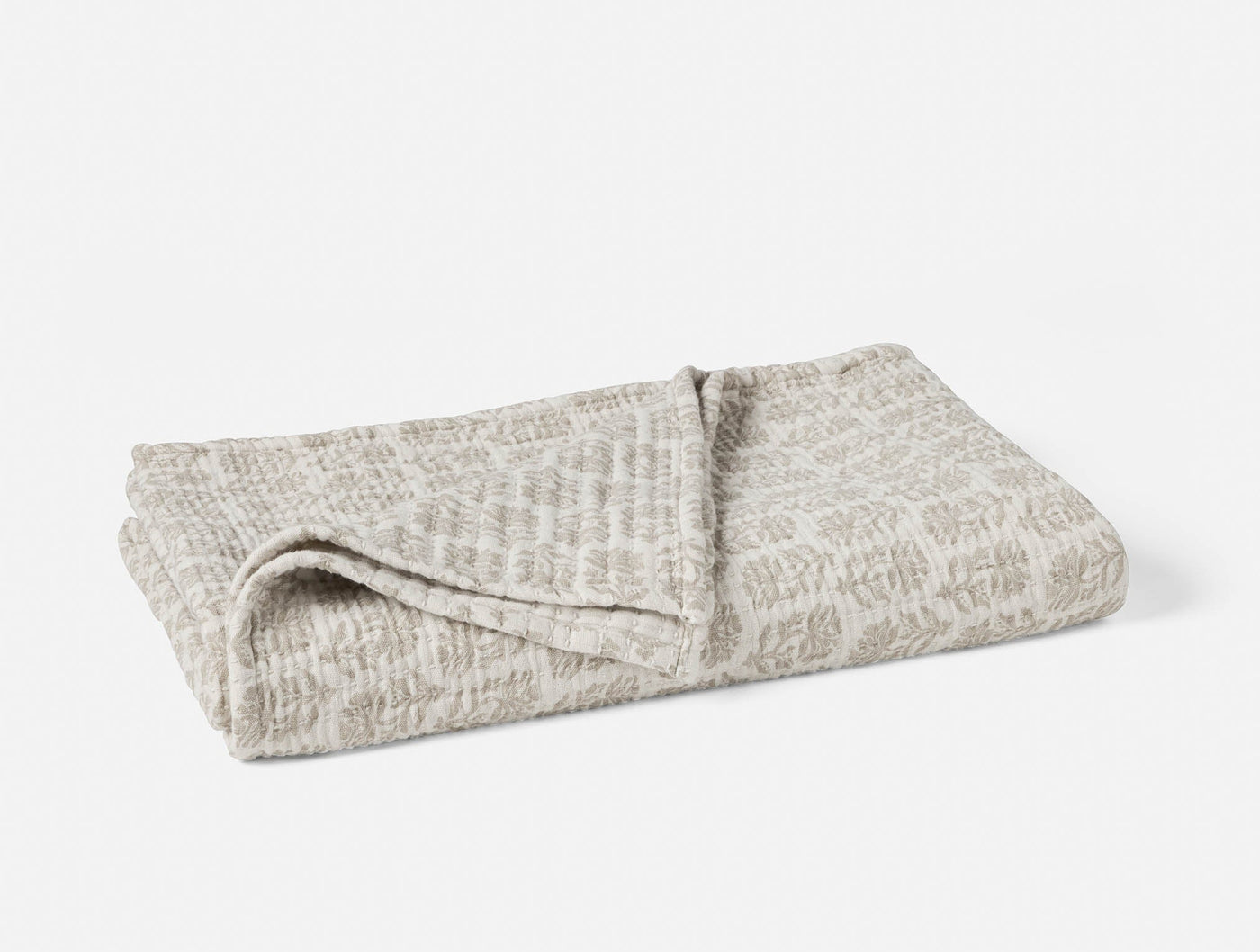 Folded Coyuchi Mirada Matelassé throw in natural, showing allover woven pattern on top surface.