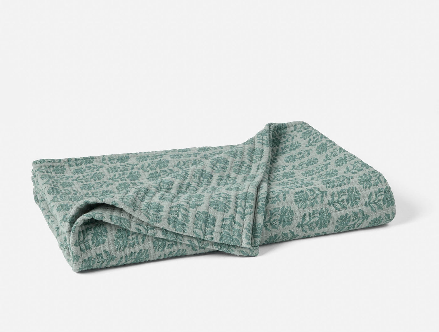 Folded sage green Coyuchi Mirada Matelasse throw with tonal botanical pattern.
