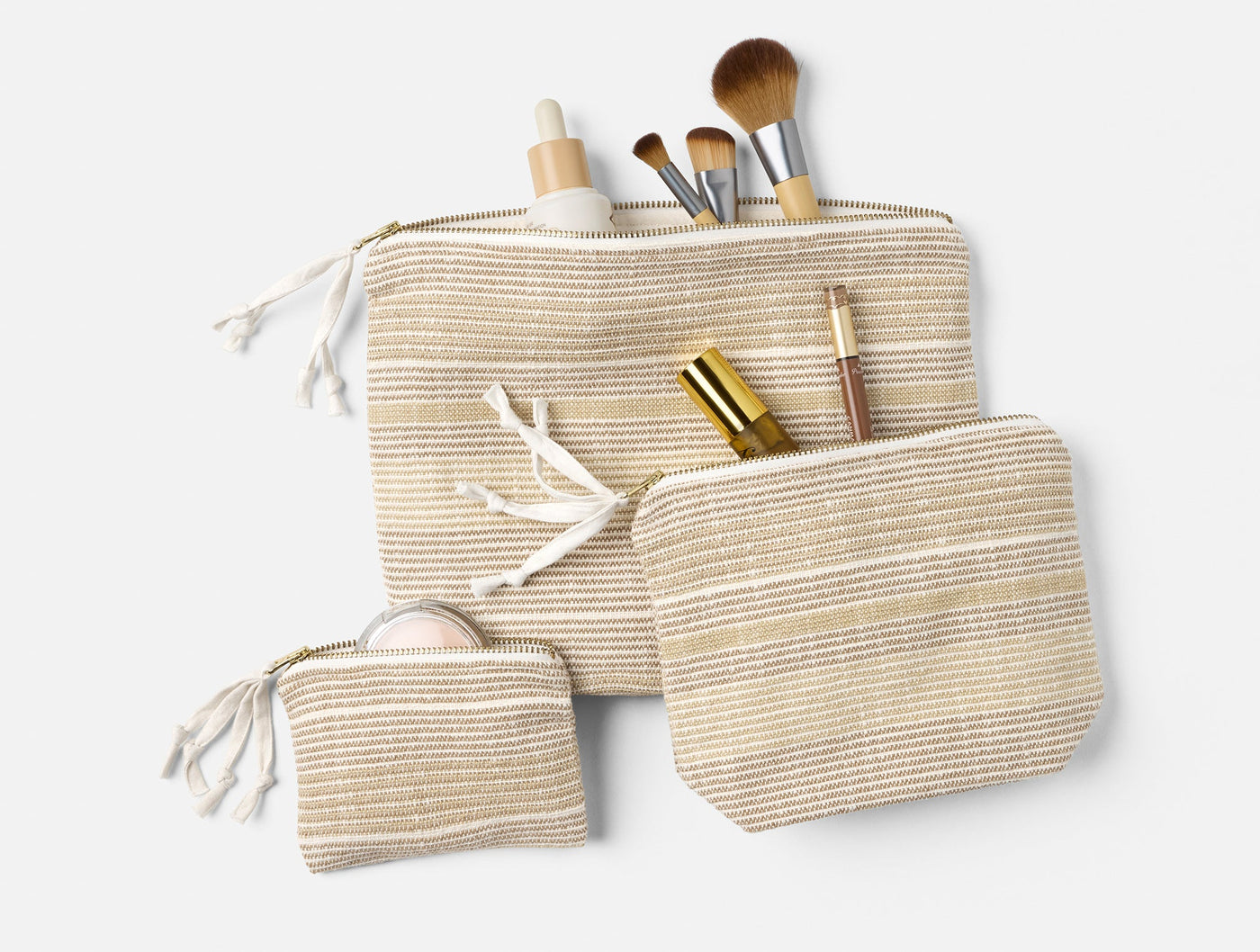 Coyuchi Miraloma pouch set of three in natural stripe, styled with makeup brushes and beauty products.