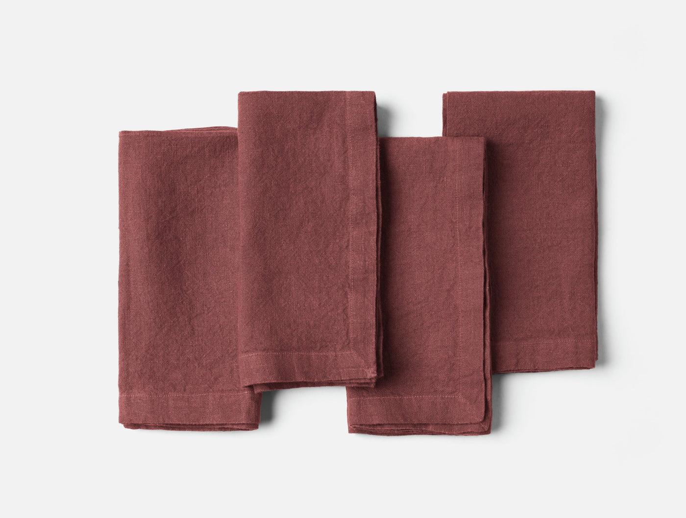 Four folded dusty rose linen napkins fanned out on a white surface.