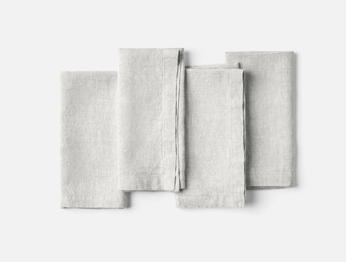 Four folded Coyuchi Mojave Linen napkins fanned flat on white background, pale grey.