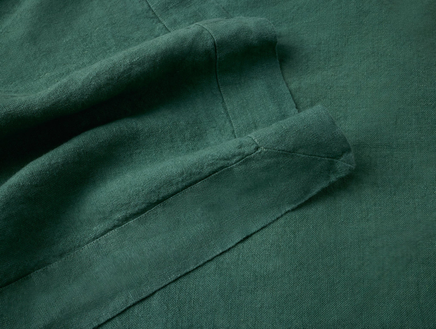Close-up of forest green linen napkin hem stitching, showing fabric drape and texture.