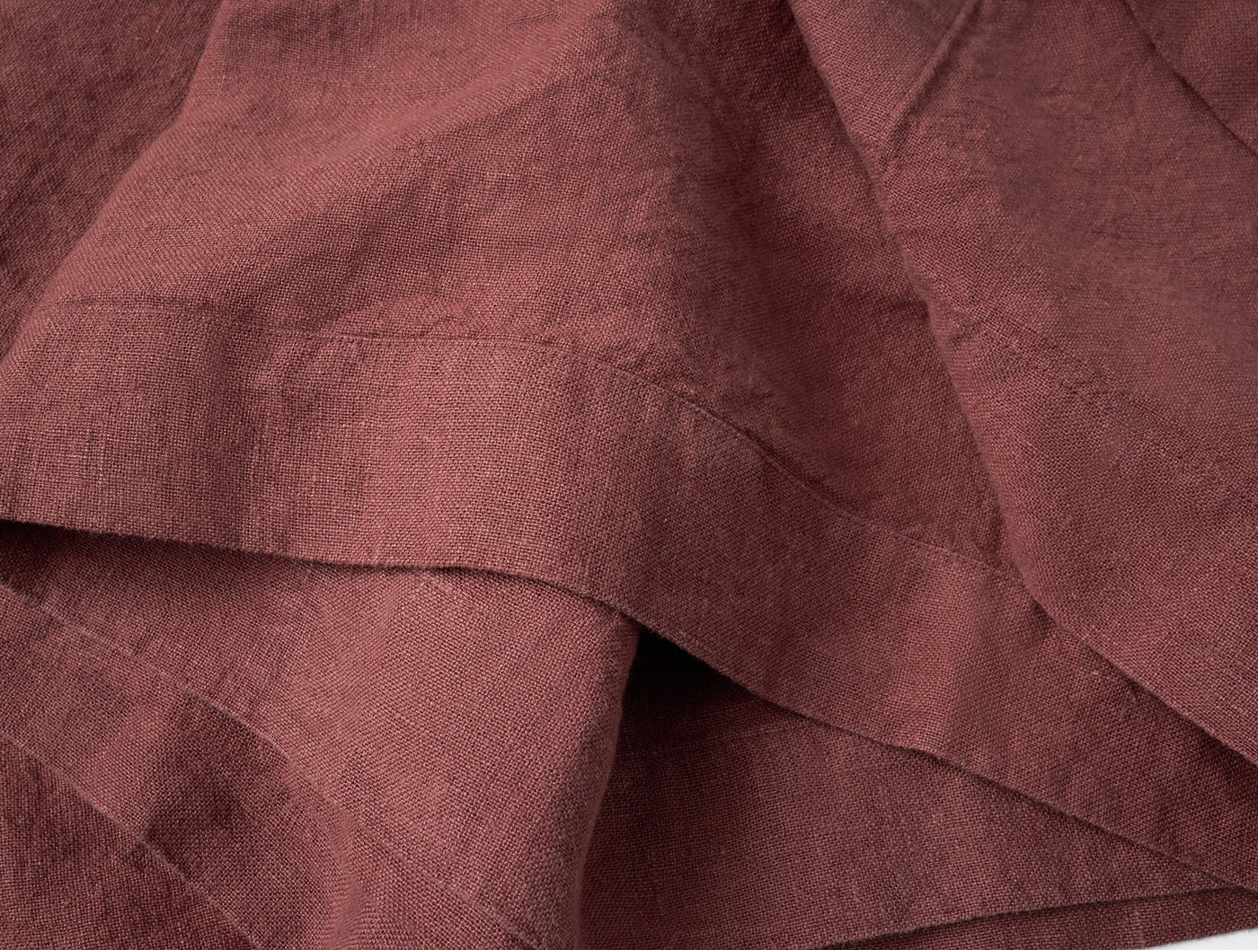 Close-up of Coyuchi Mojave linen napkin in deep burgundy, showing woven texture and hemmed edge.