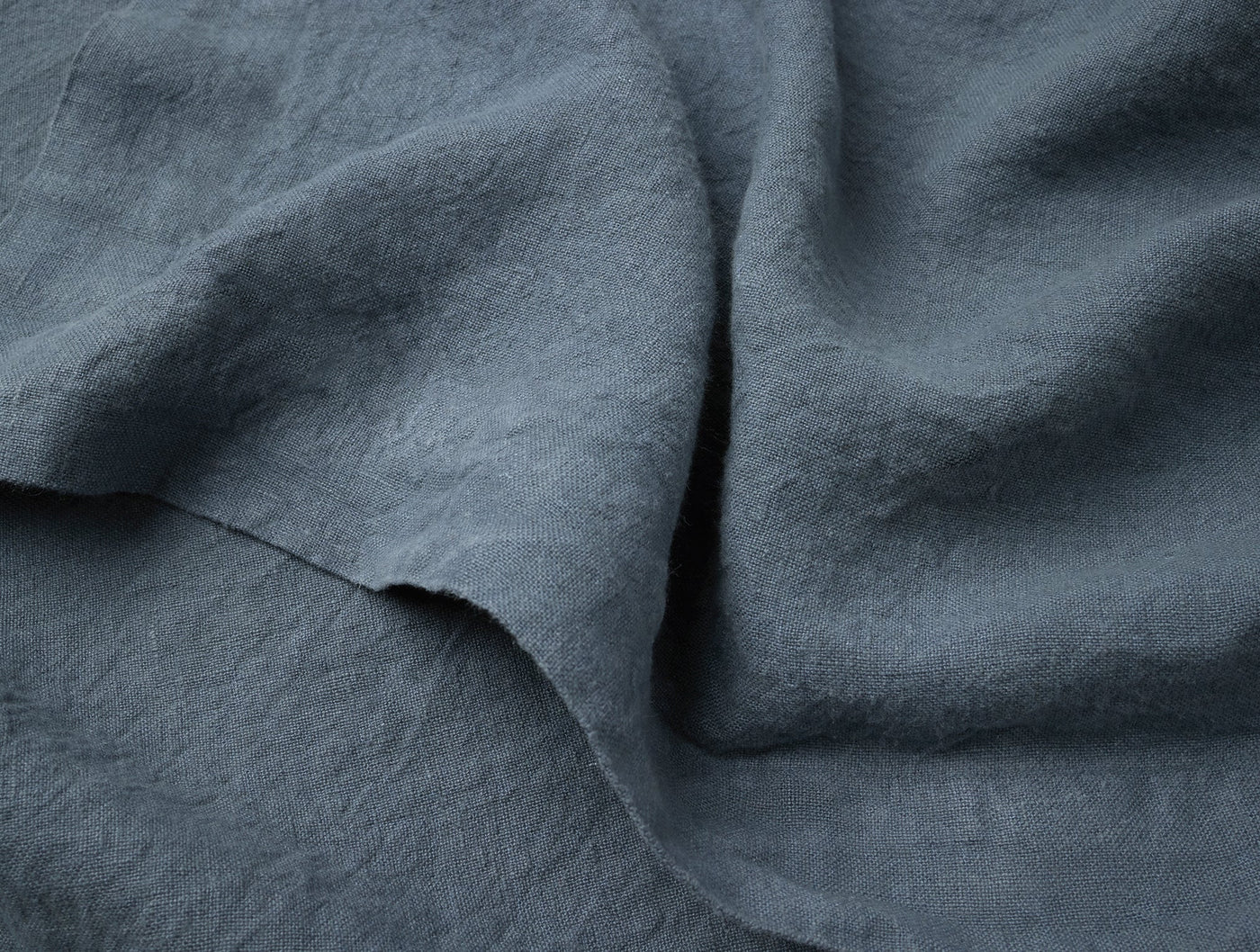 Close-up of slate blue linen napkin fabric showing relaxed texture and natural drape.
