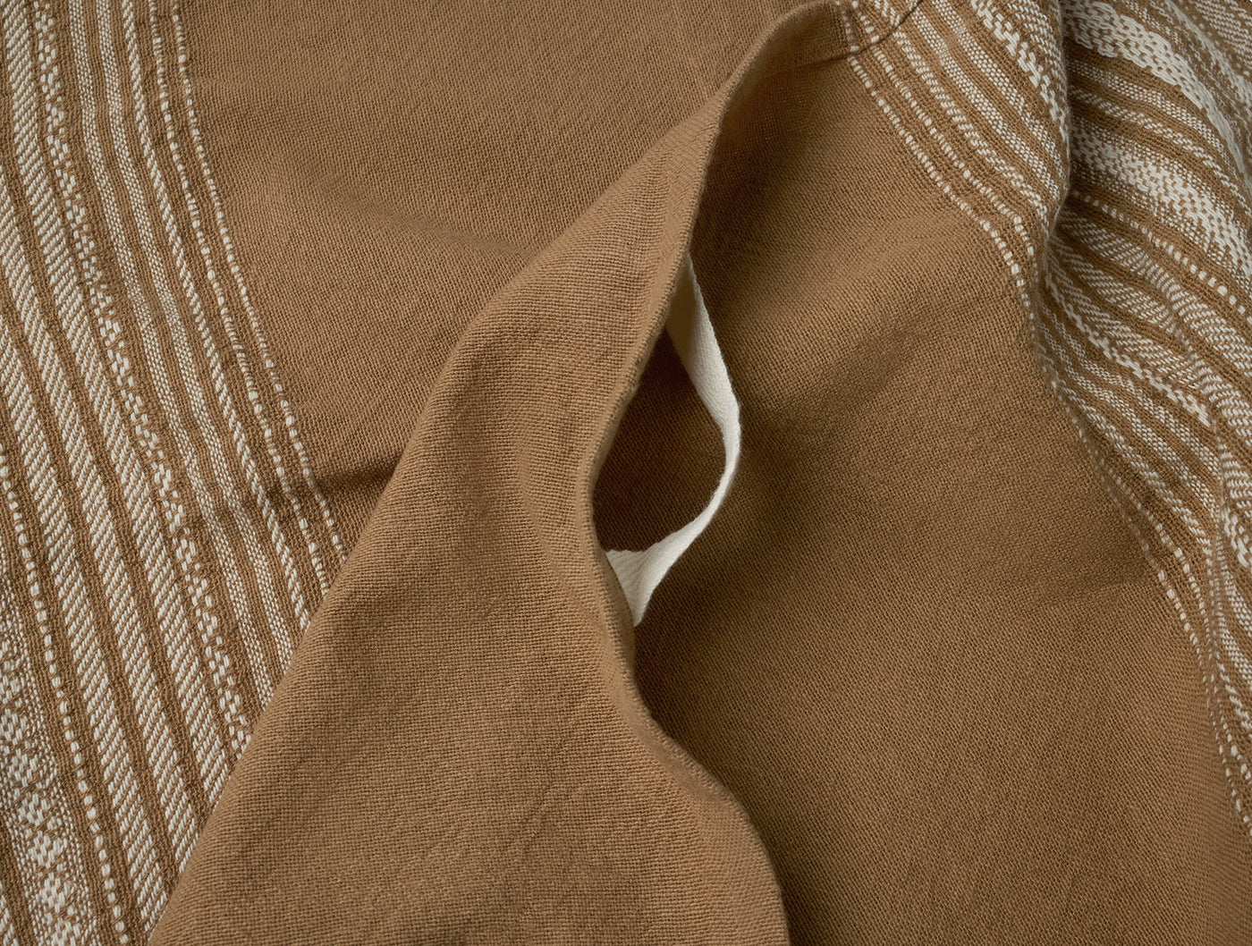 Close-up of folded caramel Coyuchi Oak hand towel showing stripe pattern and hemmed edge.