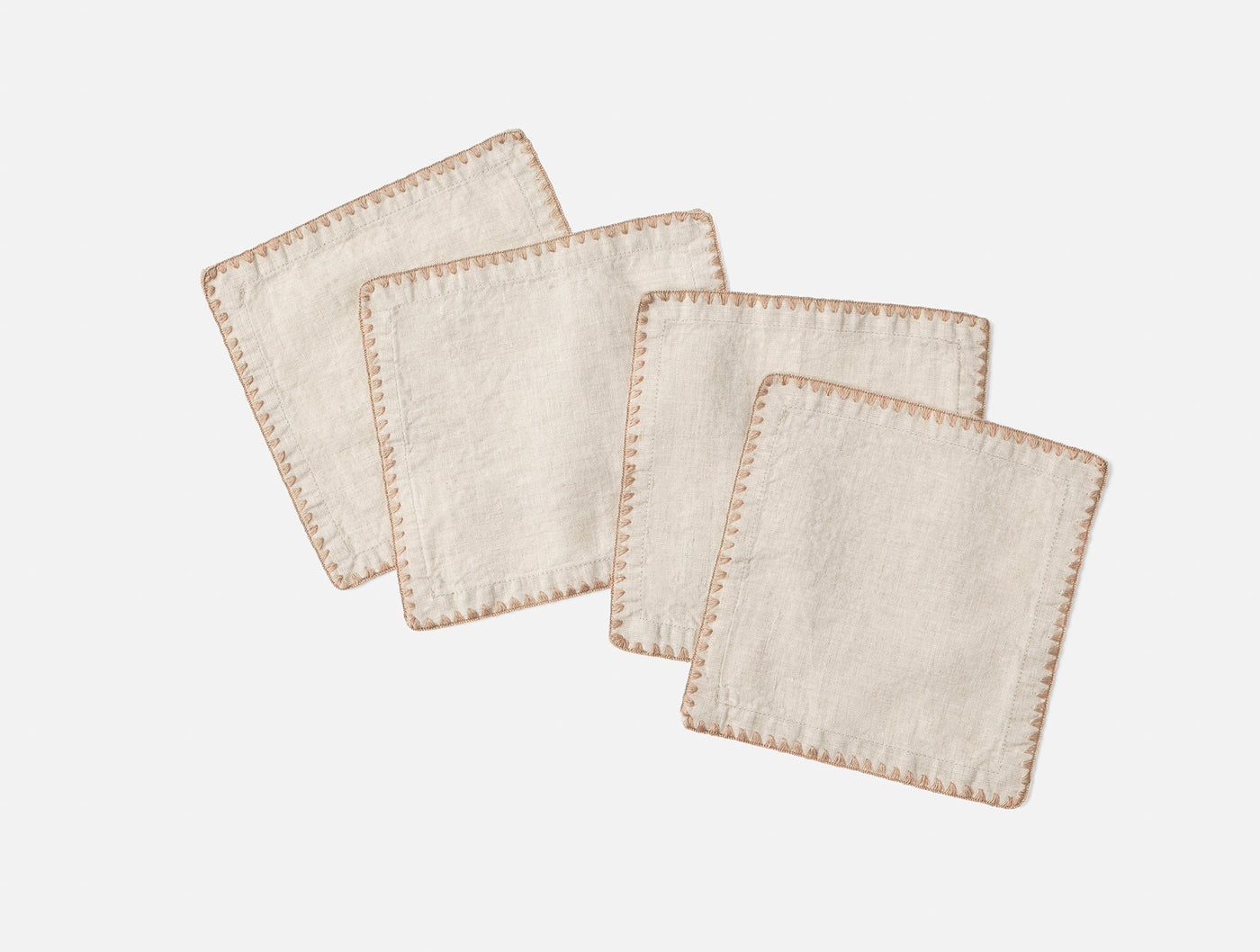 Four ivory linen cocktail napkins with tan blanket-stitch embroidered edges, fanned out on white.