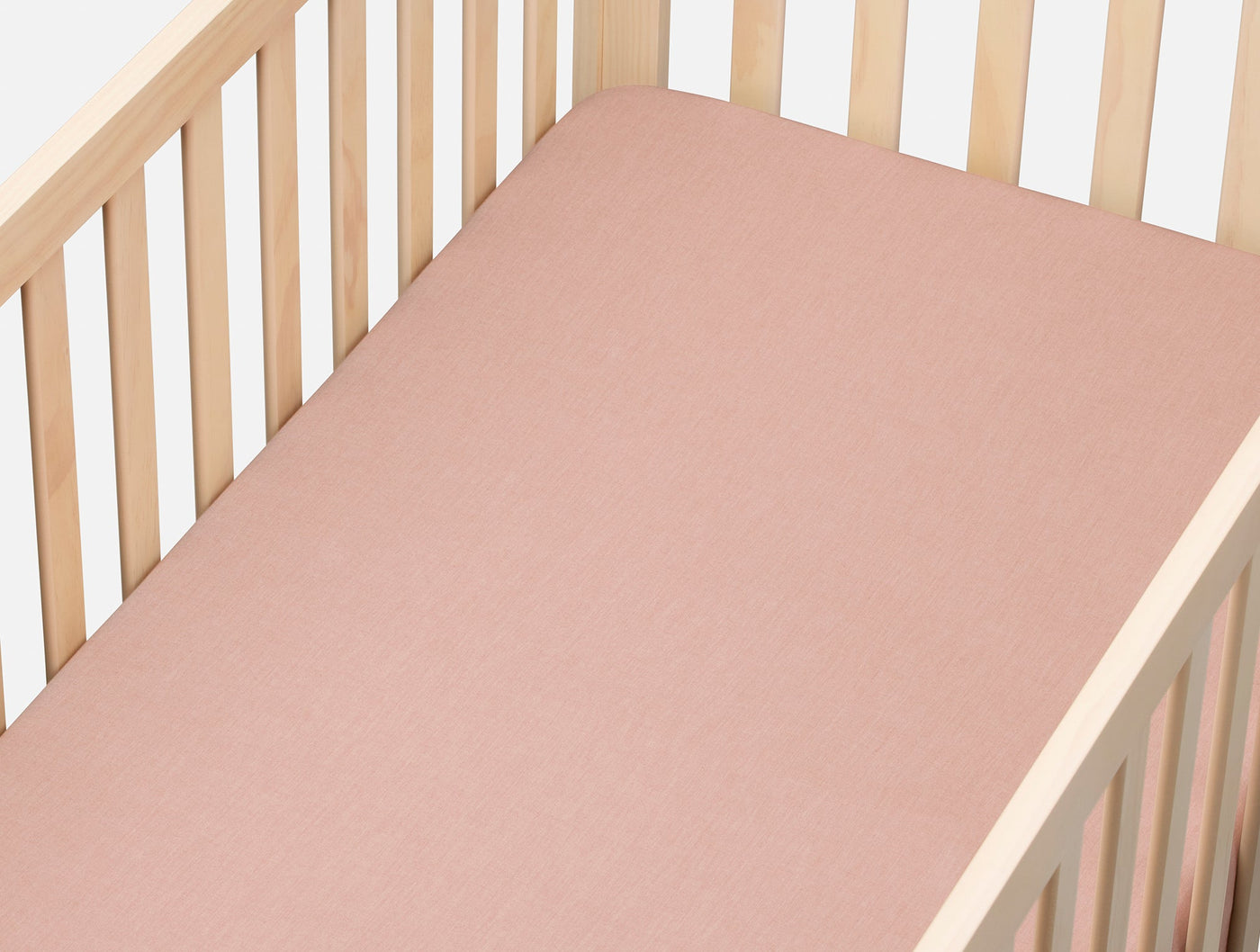Dusty rose fitted sheet on a natural wood crib, showing smooth crinkled percale texture.