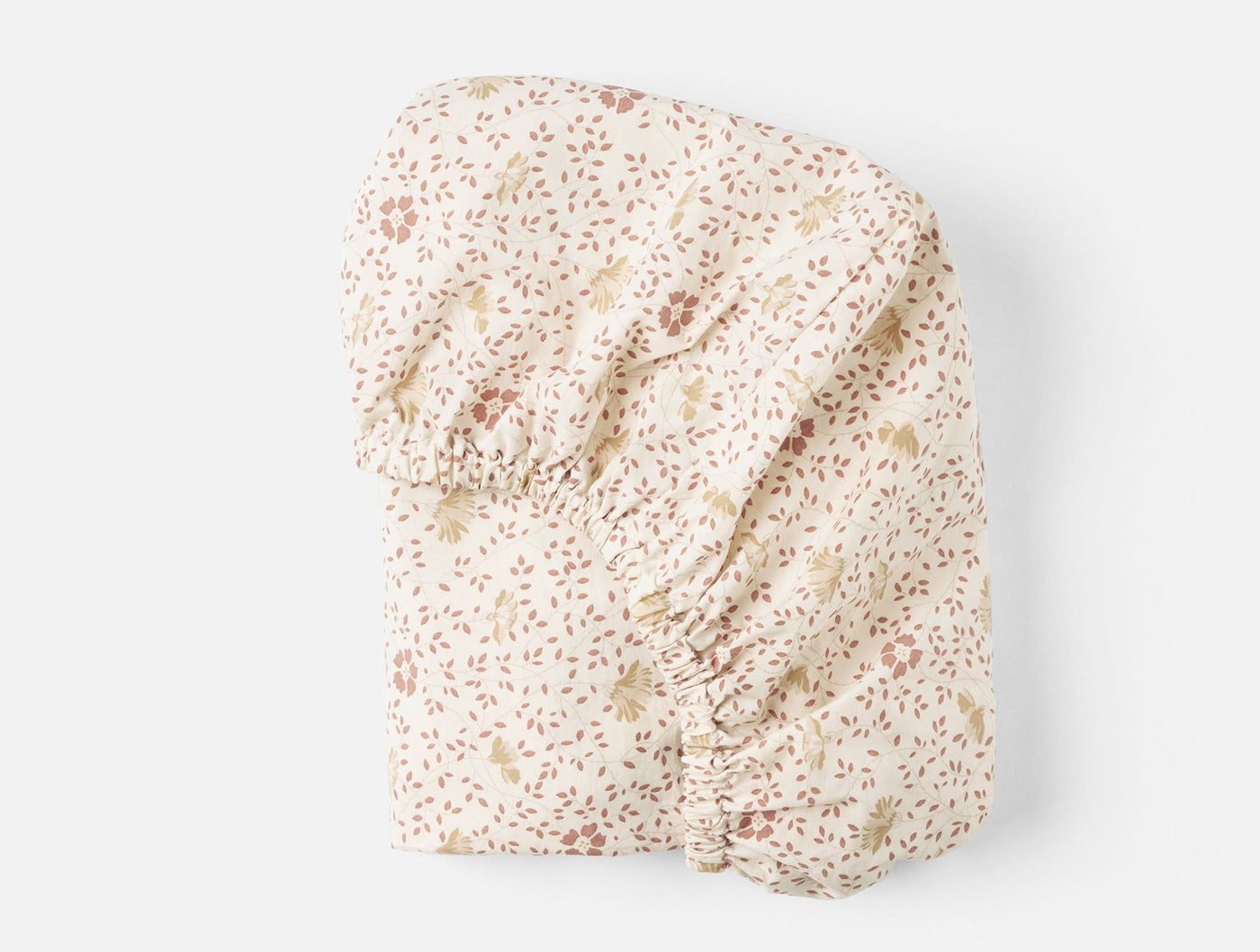 Folded ivory fitted sheet with delicate pink and gold floral print, elastic ruching visible.