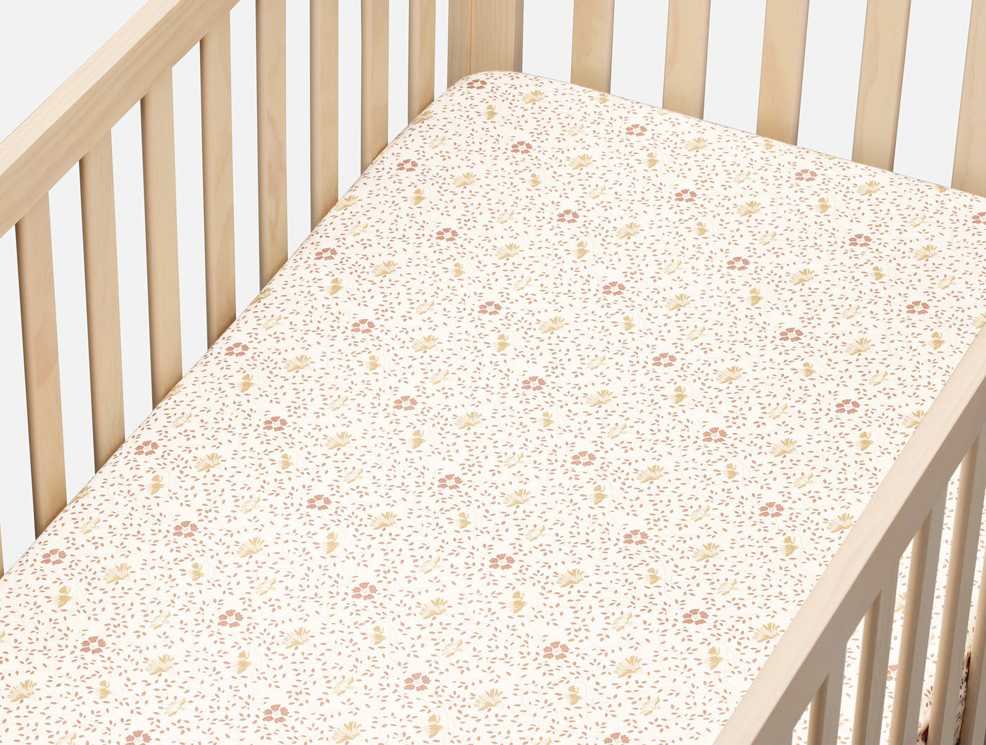 Fitted crib sheet in ivory percale with small pink and yellow floral print, styled in natural wood crib.