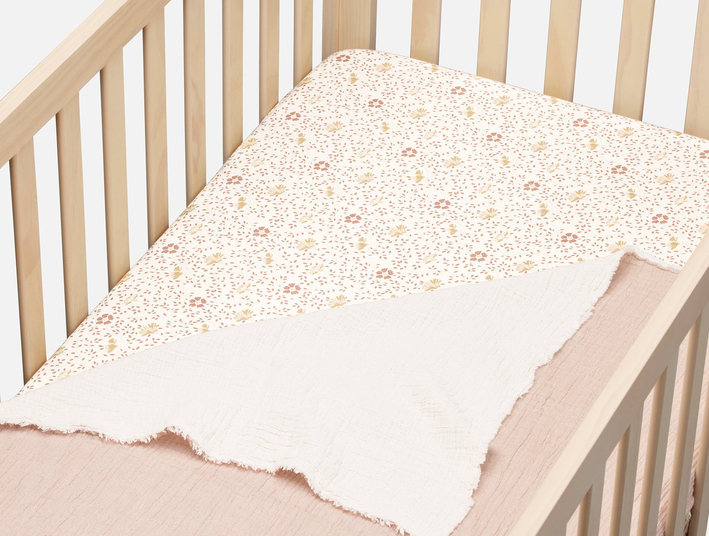 Close-up of Coyuchi fitted sheet folded back in crib, showing floral print percale over blush muslin.