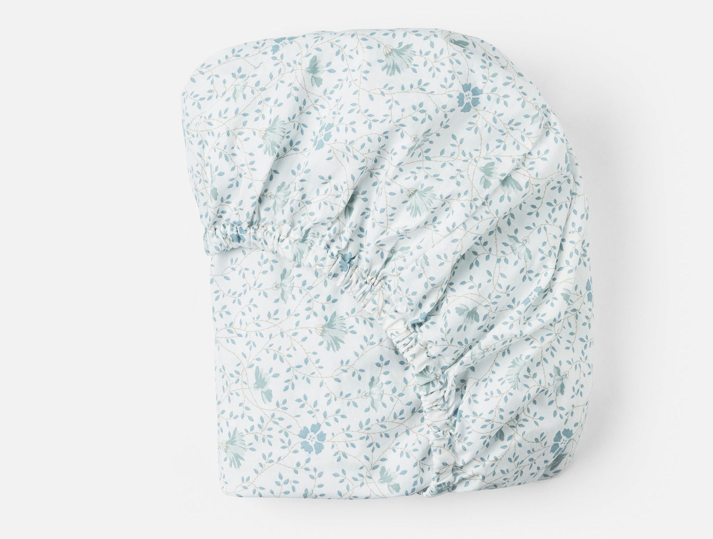 Close-up of Coyuchi fitted sheet corners with blue floral percale print on white.