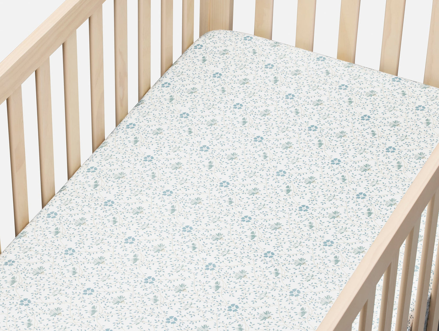 Close-up of Coyuchi fitted crib sheet with blue floral print on ivory percale.