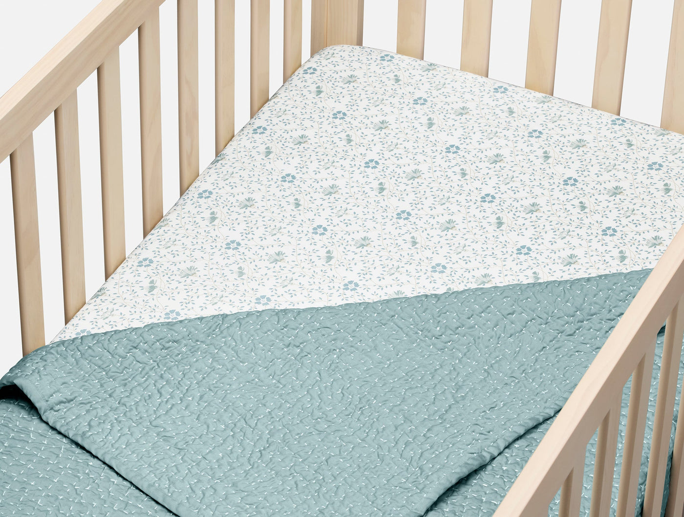 Coyuchi fitted sheet in crib, blue floral percale tucked under quilted sage coverlet.
