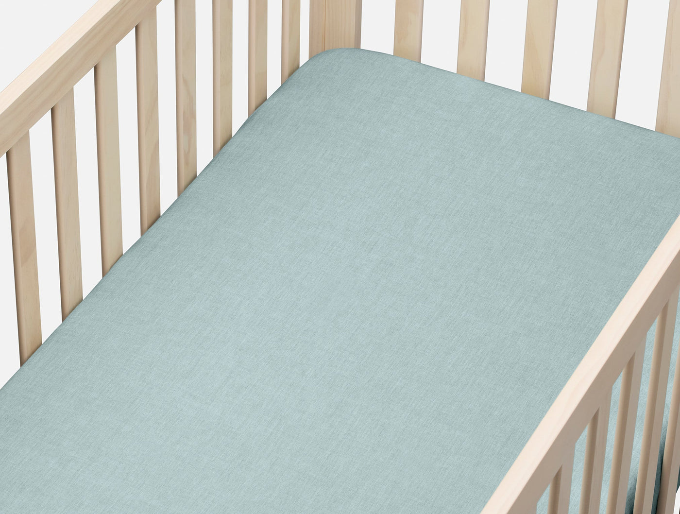 Sage-toned fitted sheet on a natural wood crib, showing subtle crinkled percale texture.