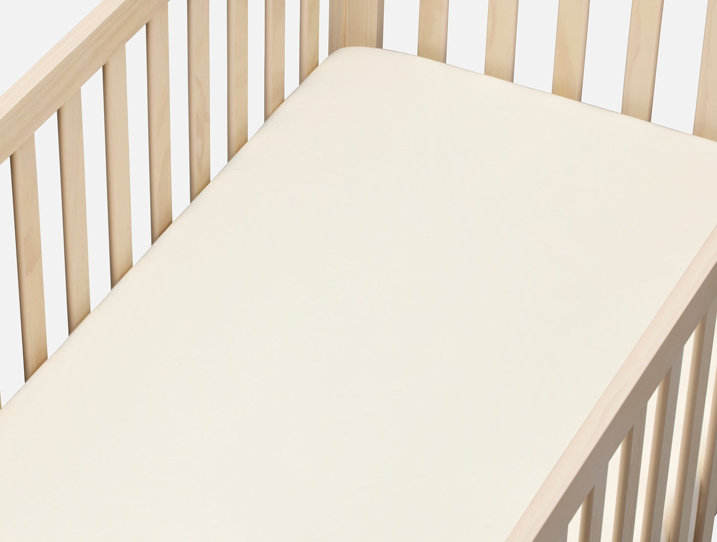 Ivory crinkled percale fitted sheet on a natural wood crib, angled overhead view.