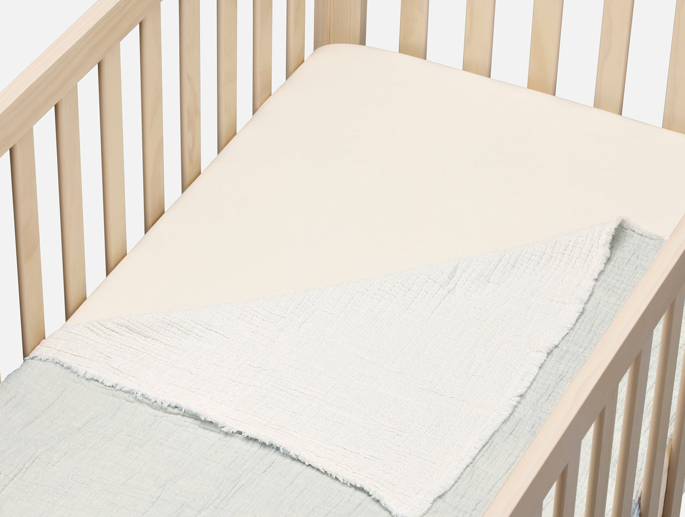 Ivory fitted sheet on a crib mattress, with a sage crinkled blanket folded at the foot.