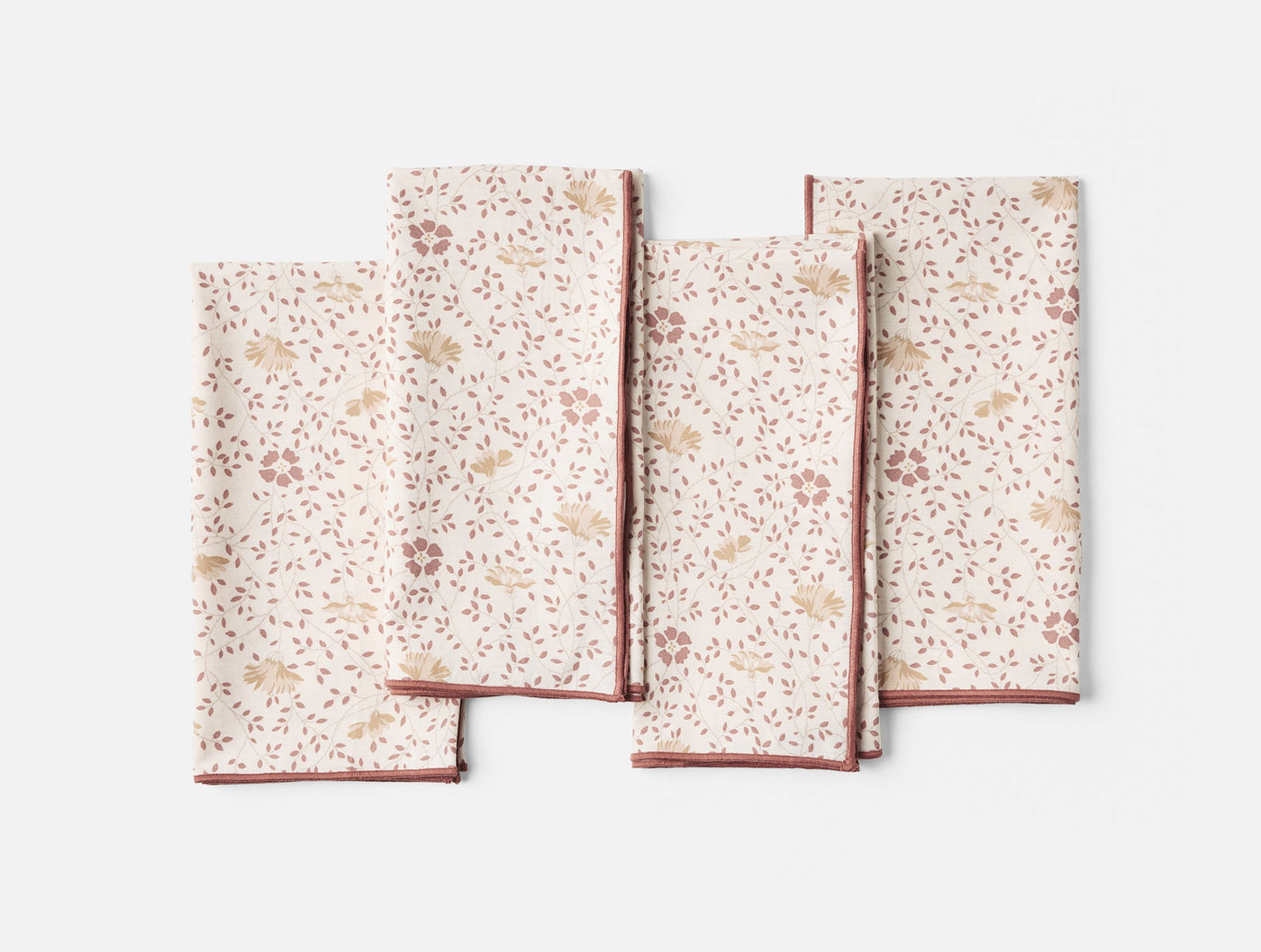 Four Coyuchi Print Percale napkins fanned flat, ivory with rose floral print and brick red trim.