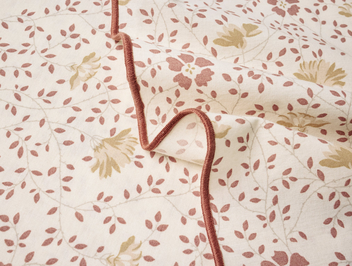 Close-up of Coyuchi ivory percale napkin with dusty rose floral and leaf print, velvet tie detail.