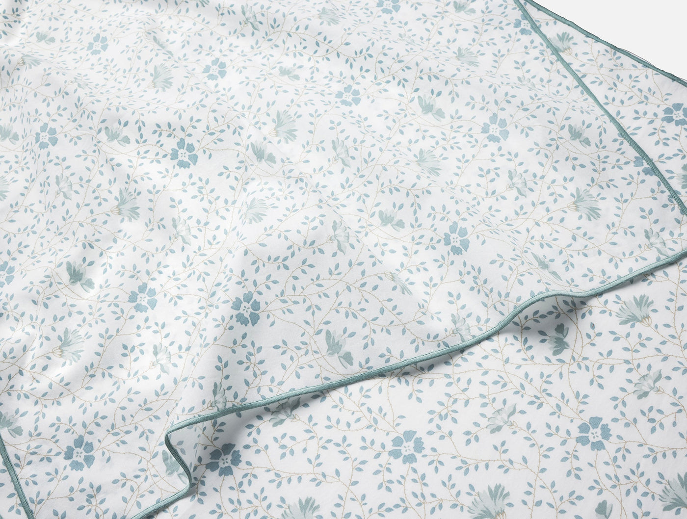 Close-up of dusty blue floral print on white percale fabric with teal piped edge detail.