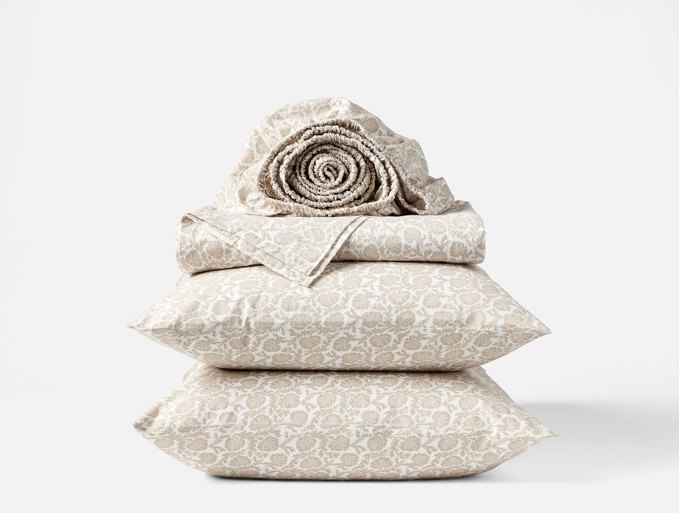Close-up of stacked Coyuchi Print Percale sheet set in taupe geometric pattern, rolled sheet on top.