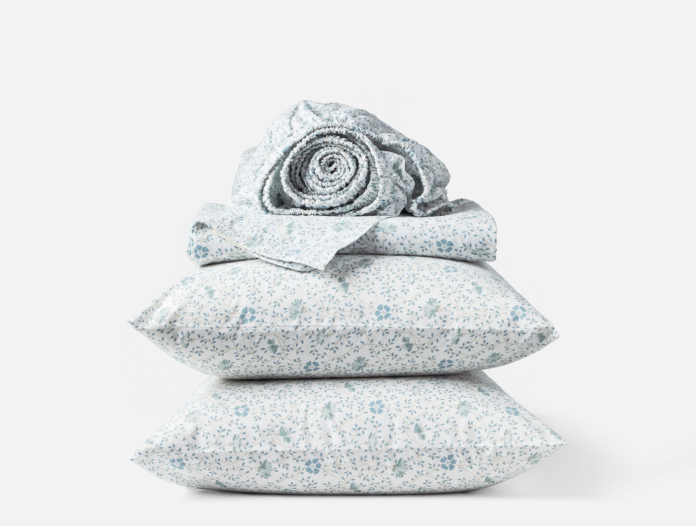 Stacked Coyuchi percale pillowcases and rolled sheet in blue floral print on white.