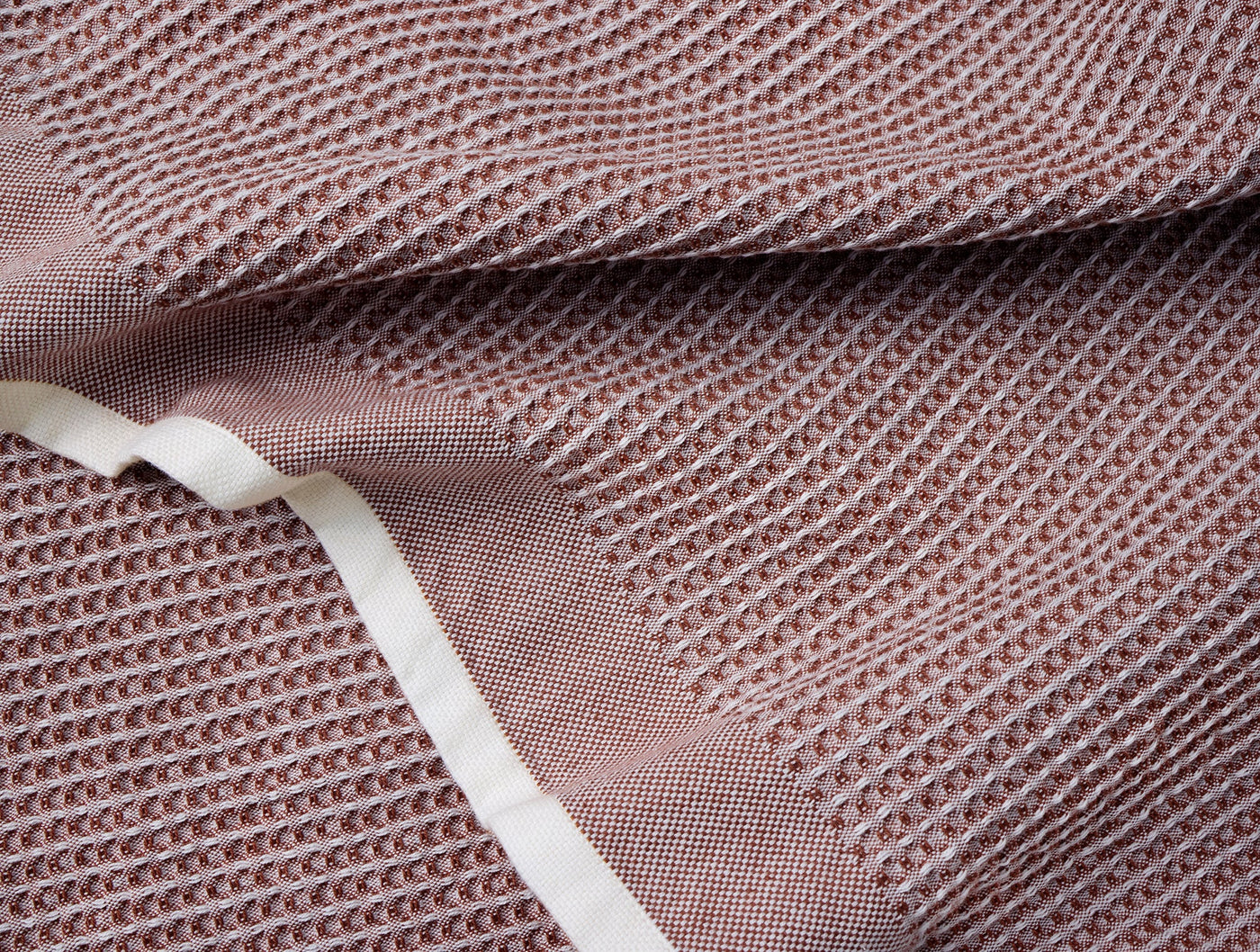Close-up of Coyuchi waffle-weave kitchen towel in dusty rose with ivory hem detail.