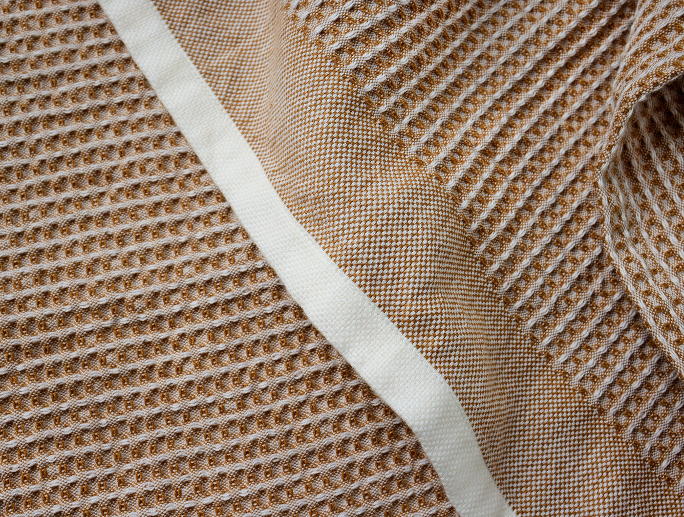 Close-up of Coyuchi waffle-weave kitchen towel in amber with ivory trim detail.