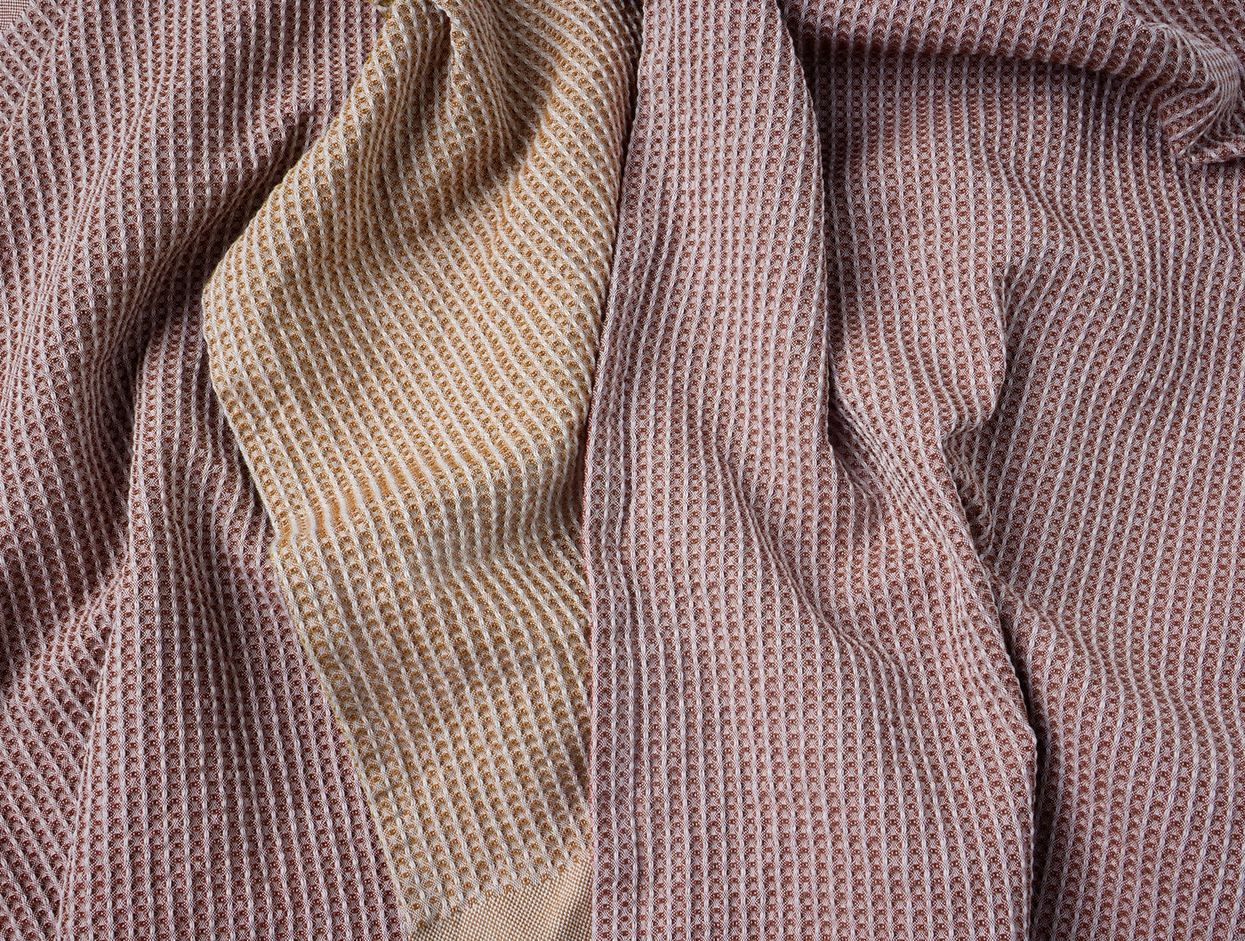 Close-up of Coyuchi Waffle kitchen towel in warm sand with red and gold woven pattern.