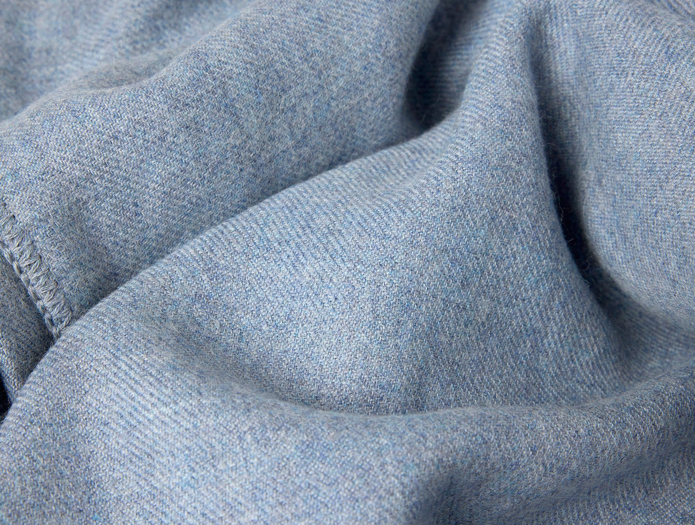 Close-up of draped sky blue baby alpaca throw, showing soft heathered weave texture.