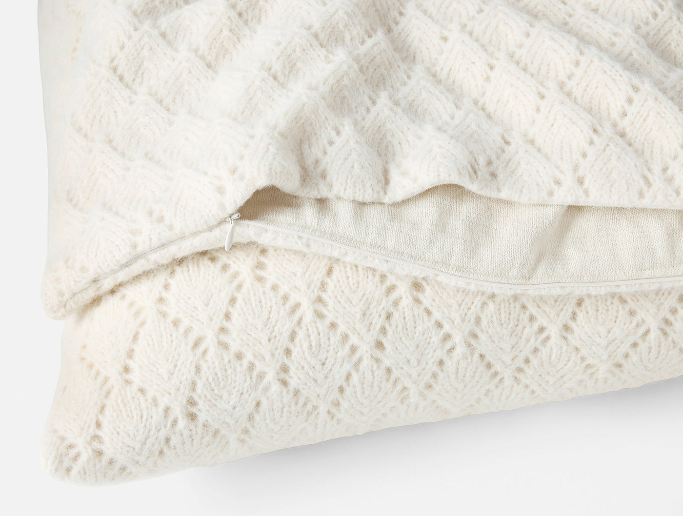 Close-up of ivory alpaca cotton knit pillow cover zipper closure and diamond lace pattern.