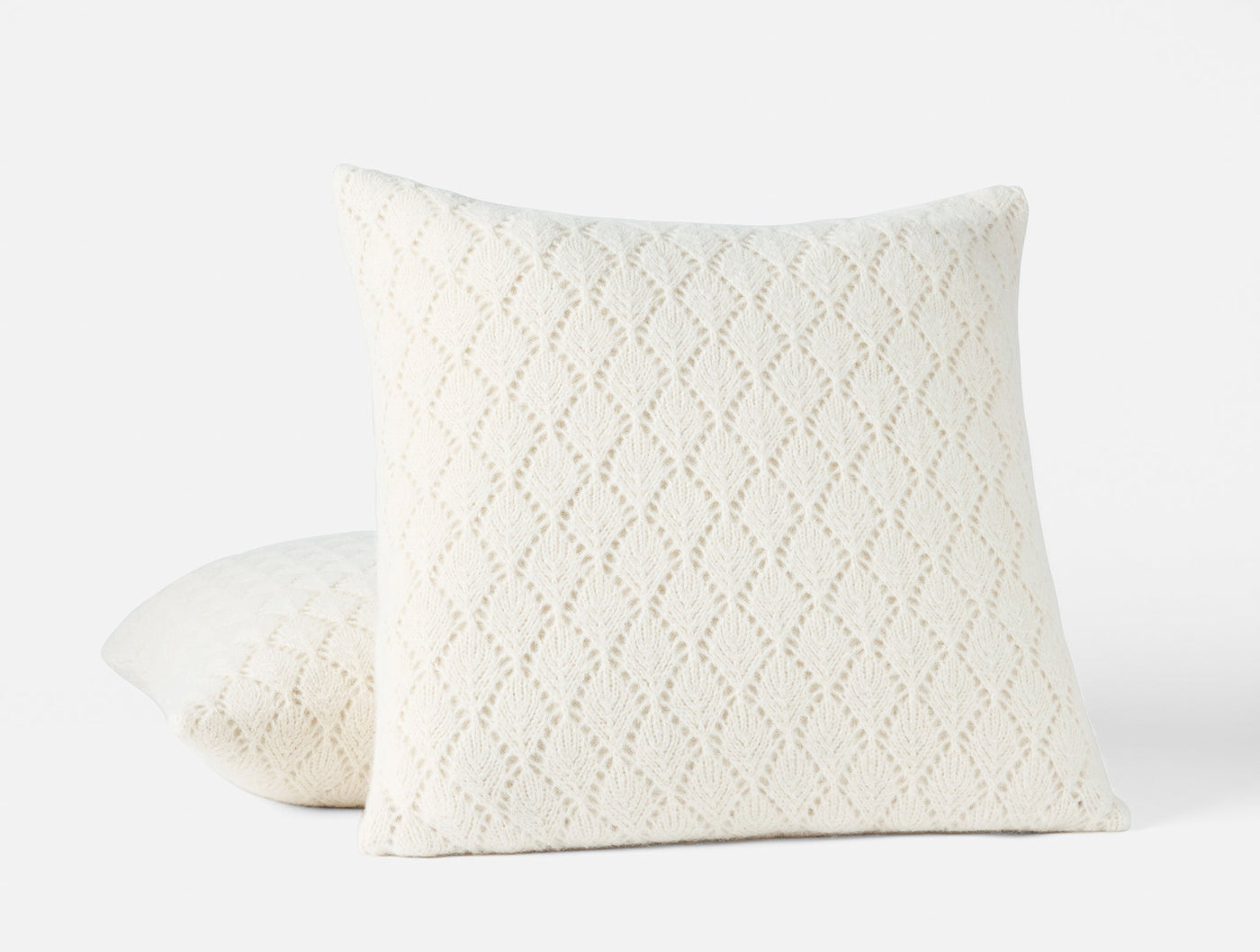 Two ivory Coyuchi Paracas pillows stacked, showing open-knit diamond pattern texture.