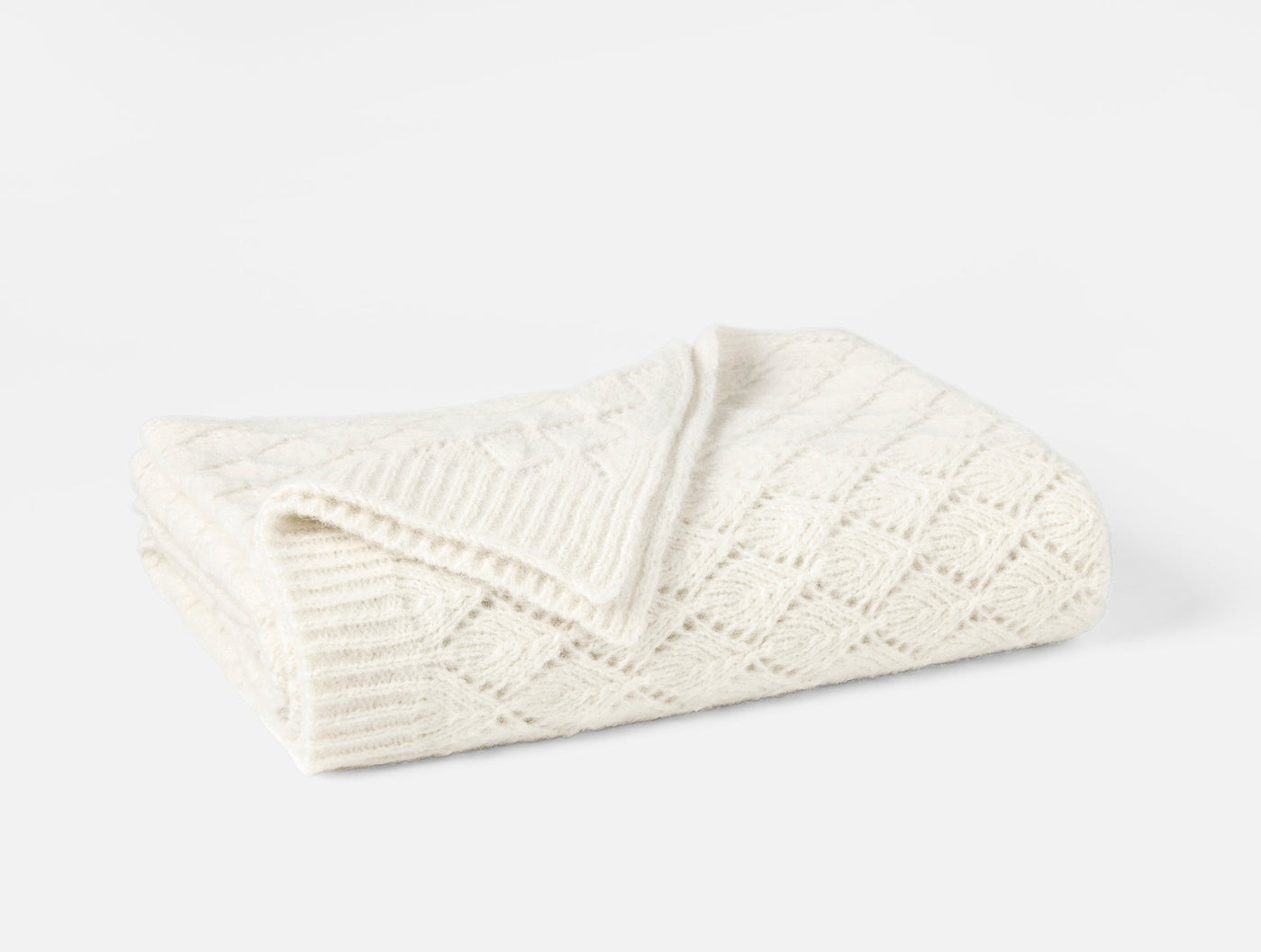 Close-up of ivory alpaca-cotton knit throw folded, showing diamond and eyelet stitch pattern.