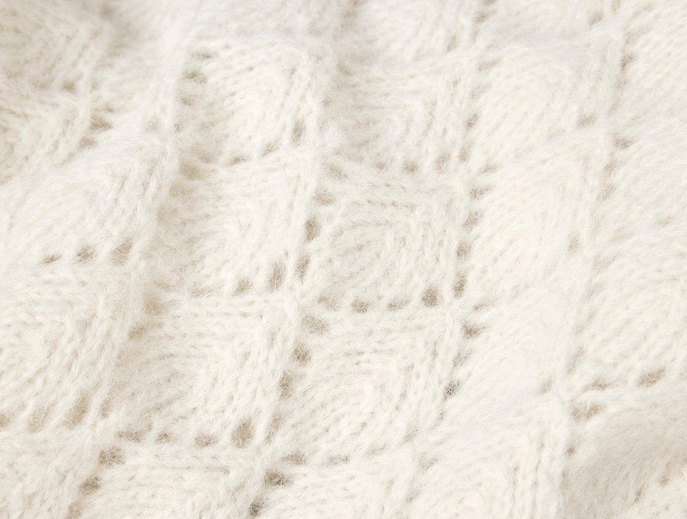 Close-up of Coyuchi Paracas throw's ivory alpaca cotton knit texture with open diamond pattern.