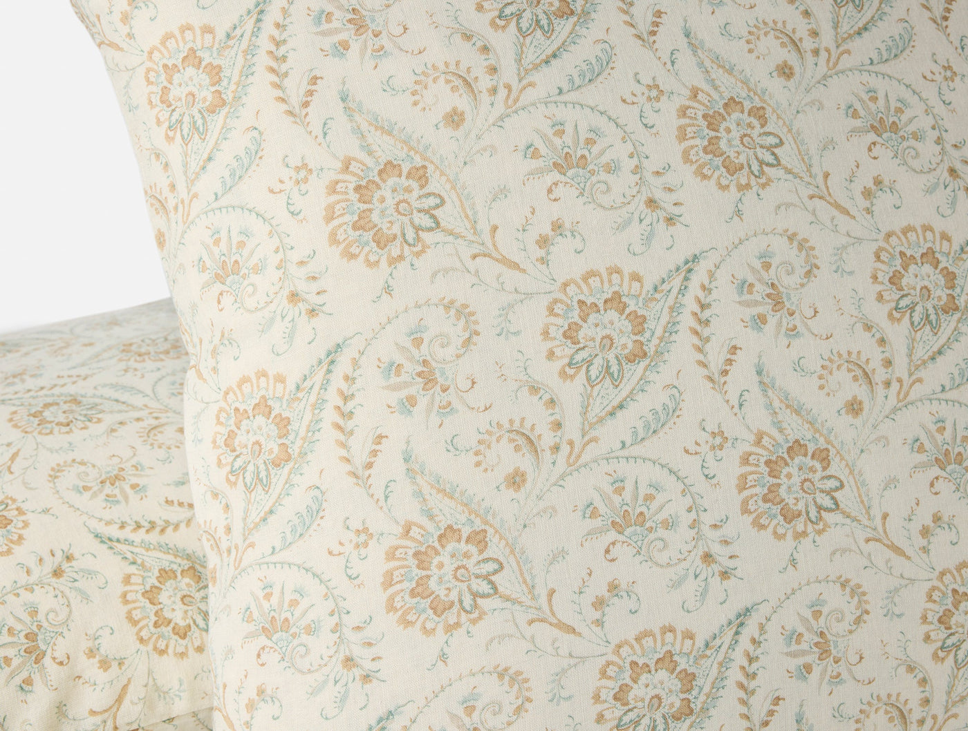 Close-up of Coyuchi Ponderosa Print pillow showing amber and sage floral motif on ivory ground.