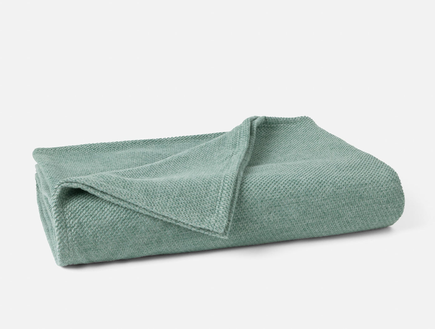 Folded sage green Coyuchi Sequoia blanket showing textured knit weave detail.