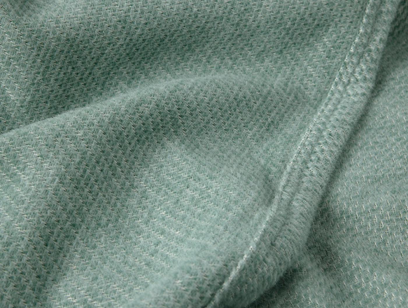 Close-up of sage green Coyuchi Sequoia throw showing textured weave and stitched hem detail.