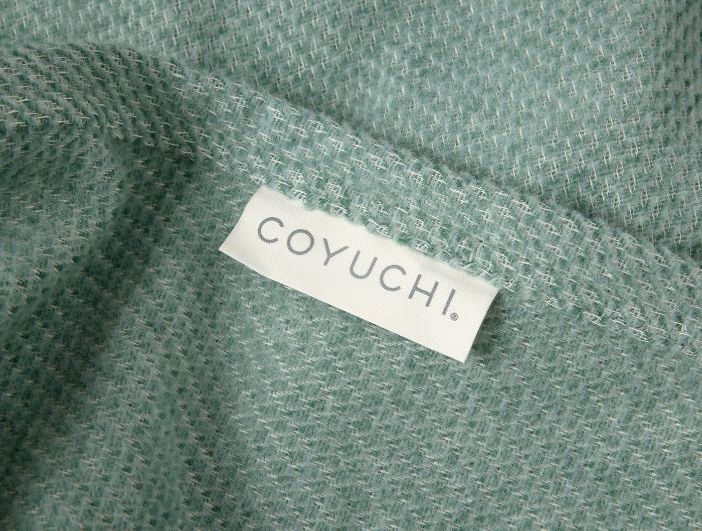 Close-up of Coyuchi Sequoia throw in sage green, showing woven texture and woven label.