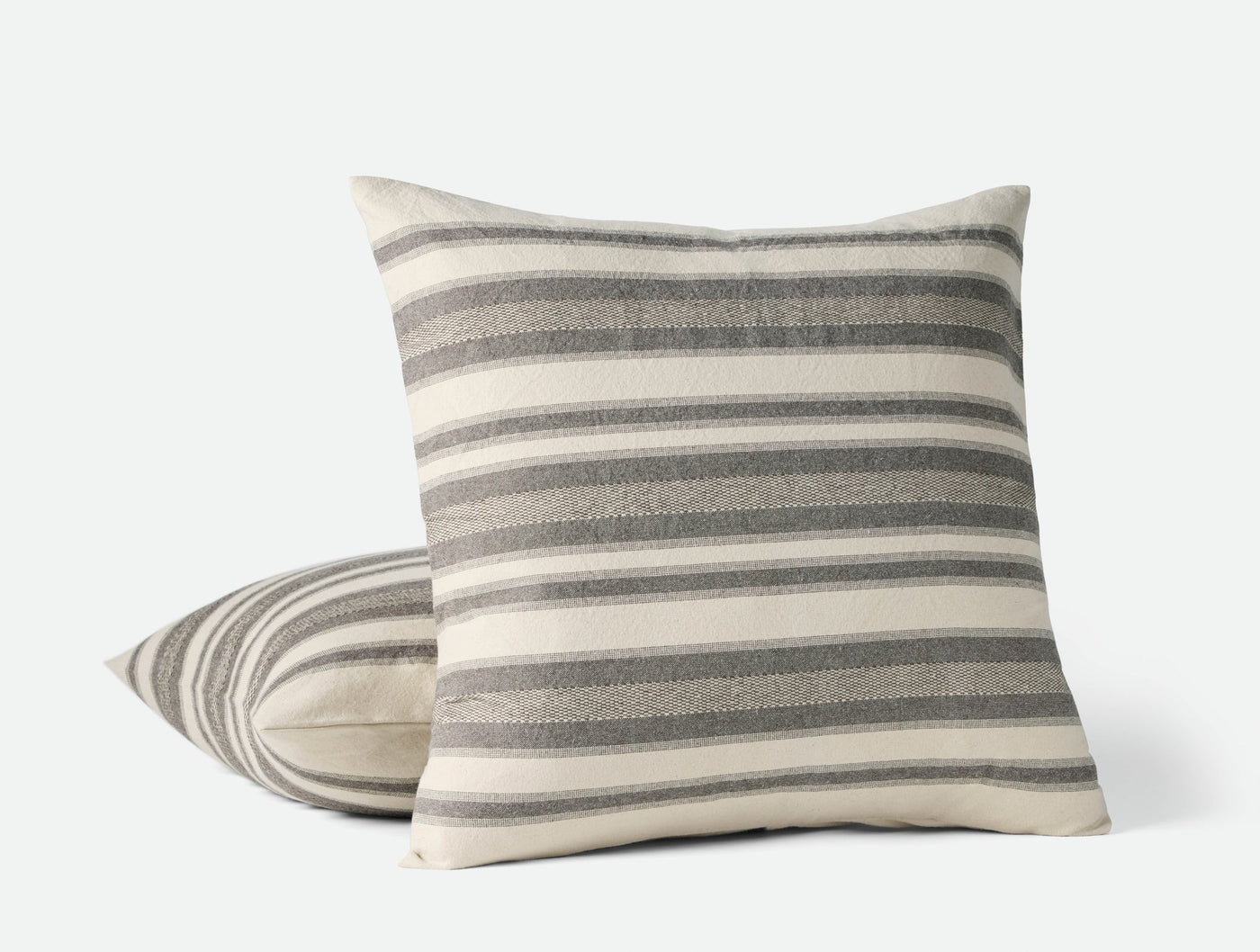 Two Coyuchi Serrano pillows stacked, ivory and grey woven stripes, textured linen front face.