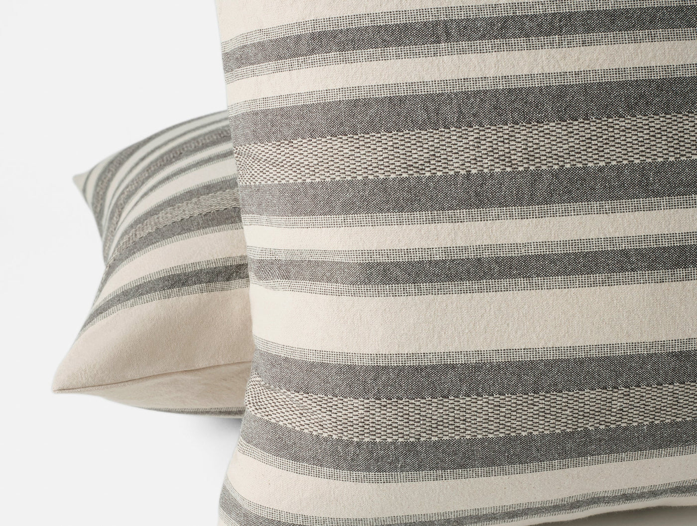 Close-up of Coyuchi Serrano pillow covers stacked, showing charcoal and ivory stripe weave detail.