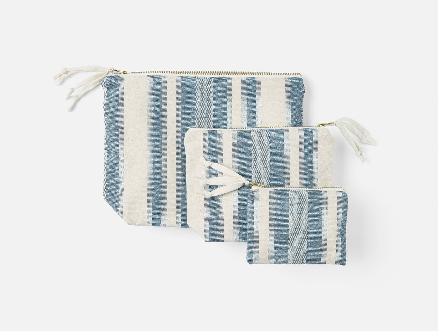Three Coyuchi Serrano pouches in varied sizes, blue and ivory stripe with gold zippers.