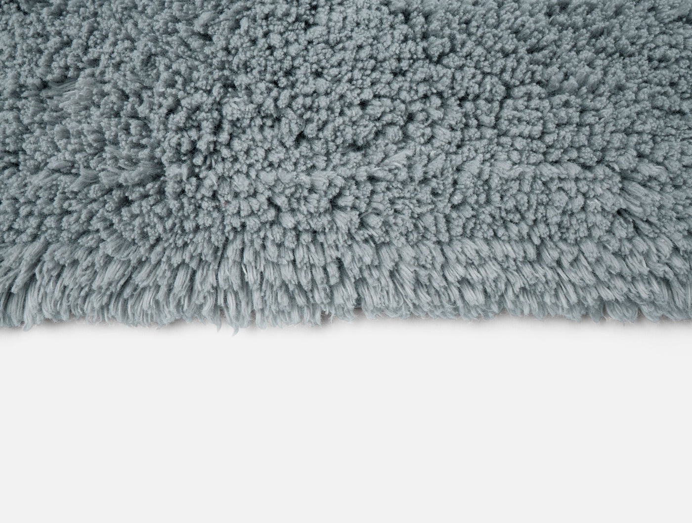 Close-up of Coyuchi Shag bath rug edge in slate blue, showing dense looped texture.