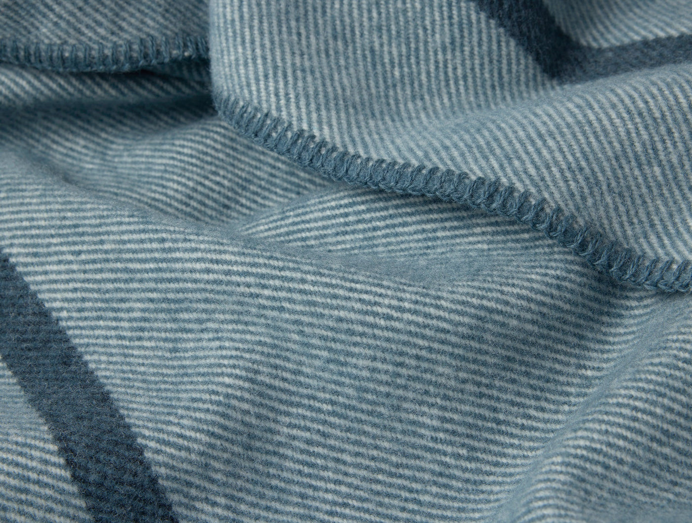 Close-up of Coyuchi Tahoe Wool blanket hem with teal herringbone weave and stripe detail.