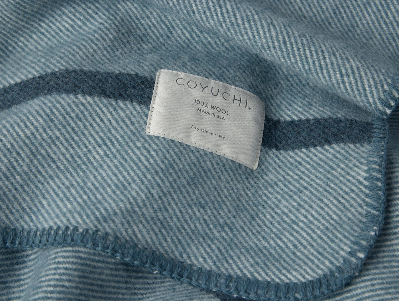 Close-up of Coyuchi Tahoe Wool throw care label on slate blue herringbone wool fabric.
